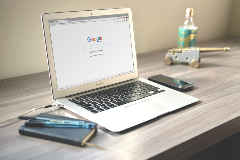 Laptop met de Google-zoekpagina op een bureau, naast een smartphone en notitieboek