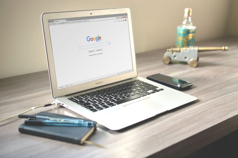 Laptop met de Google-zoekpagina op een bureau, naast een smartphone en notitieboek